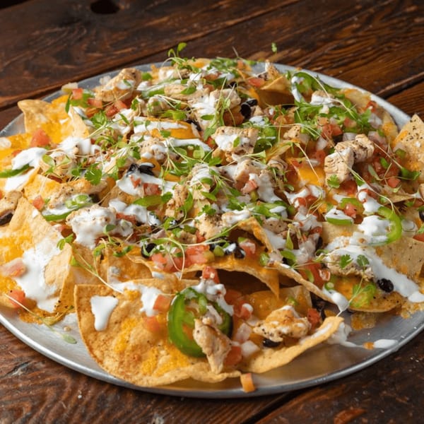A large platter of Press Box Sports Grill nachos with chicken, cheese, salsa, jalapeños, and sour cream.
