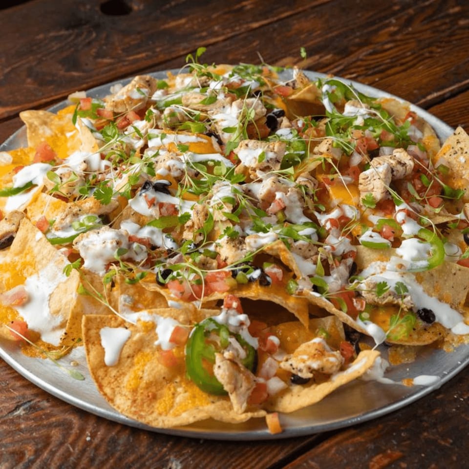 A large platter of Press Box Sports Grill nachos with chicken, cheese, salsa, jalapeños, and sour cream.