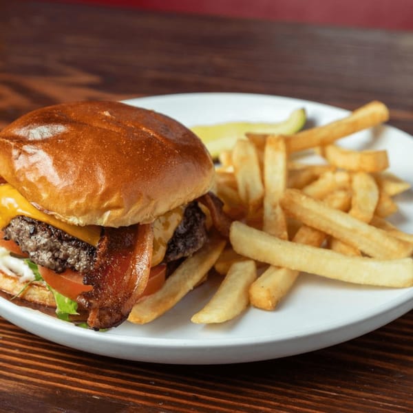 A bacon cheeseburger with lettuce, tomato, and a side of golden fries on a white plate.