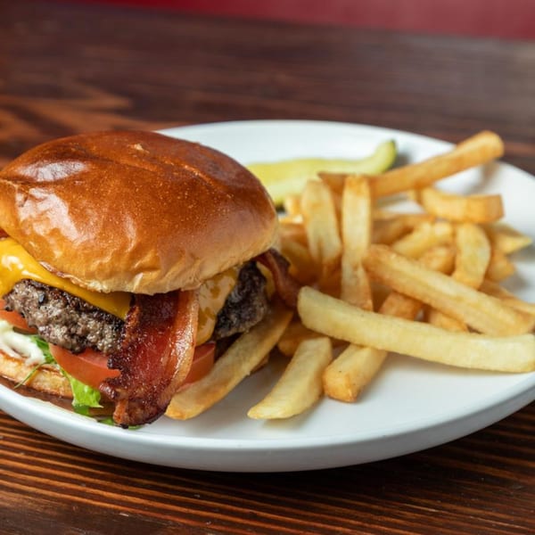 Bacon cheeseburger with lettuce, tomato, and fries on a white plate at Press Box Sports Grill.