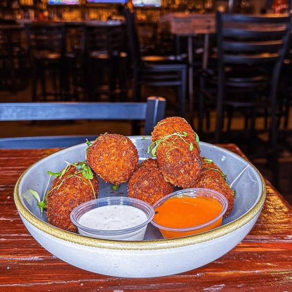 Crispy fried appetizers with microgreens and dipping sauces in a bowl on a wooden table at Press Box Sports Grill.