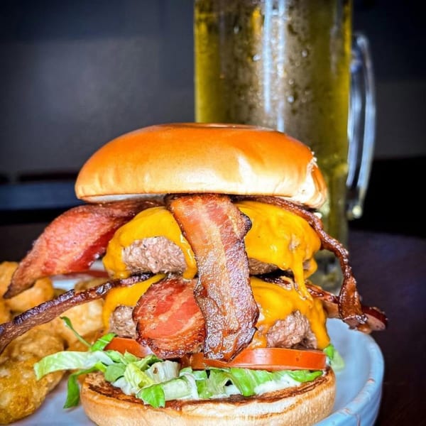 A double bacon cheeseburger with lettuce, tomato, and a side of fries and beer.