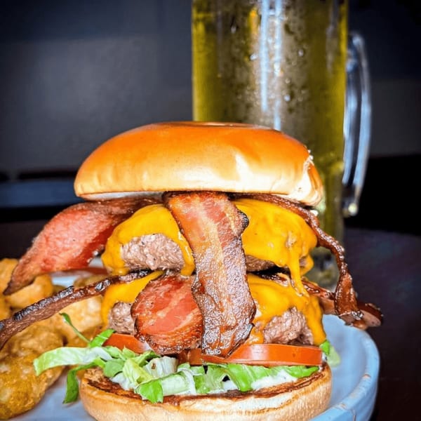 A double bacon cheeseburger with lettuce and tomato, served with fries and a beer.